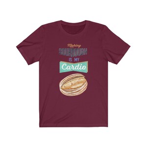 May include: A maroon t-shirt with the text "Making sourdough is my cardio" in a vintage style font. A cartoon image of a sourdough loaf is below the text.