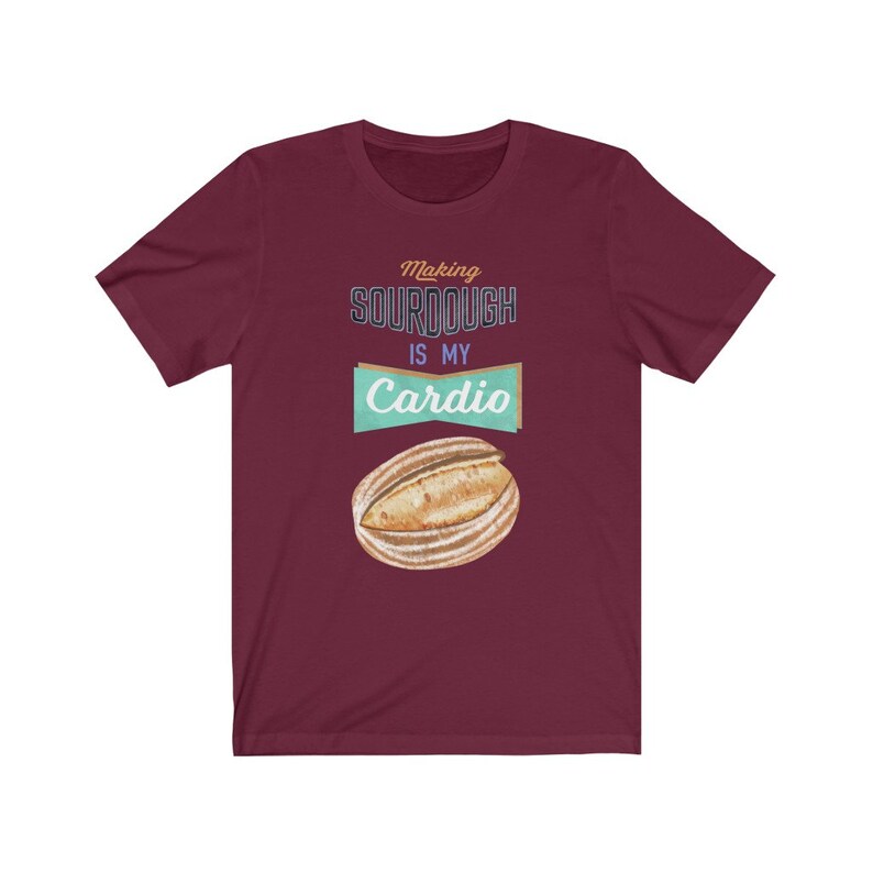 May include: A maroon t-shirt with the text "Making sourdough is my cardio" in a vintage style font. A cartoon image of a sourdough loaf is below the text.