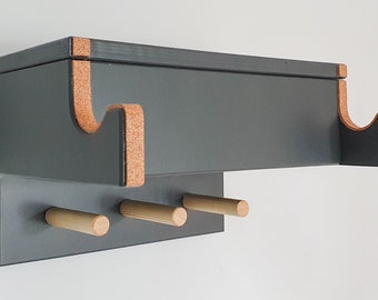 May include: A dark grey wooden wall-mounted shelf with cork accents and three wooden pegs. The shelf has two curved cutouts on the top for hanging items.