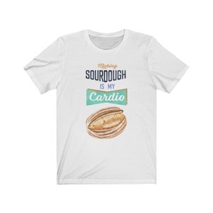 May include: White t-shirt with the text "Making sourdough is my cardio" in blue and brown text. A cartoon loaf of sourdough bread is below the text.
