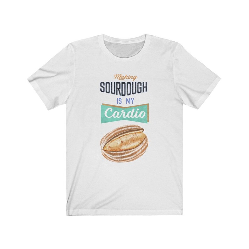 May include: White t-shirt with the text "Making sourdough is my cardio" in blue and brown text. A cartoon loaf of sourdough bread is below the text.