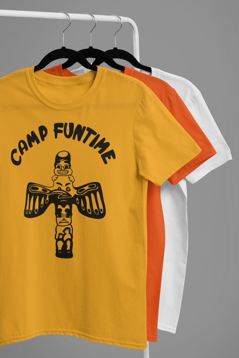 May include: Three t-shirts on hangers, the front one is yellow with a black graphic of a totem pole and the text "Camp Funtime". The middle shirt is orange and the back shirt is white.