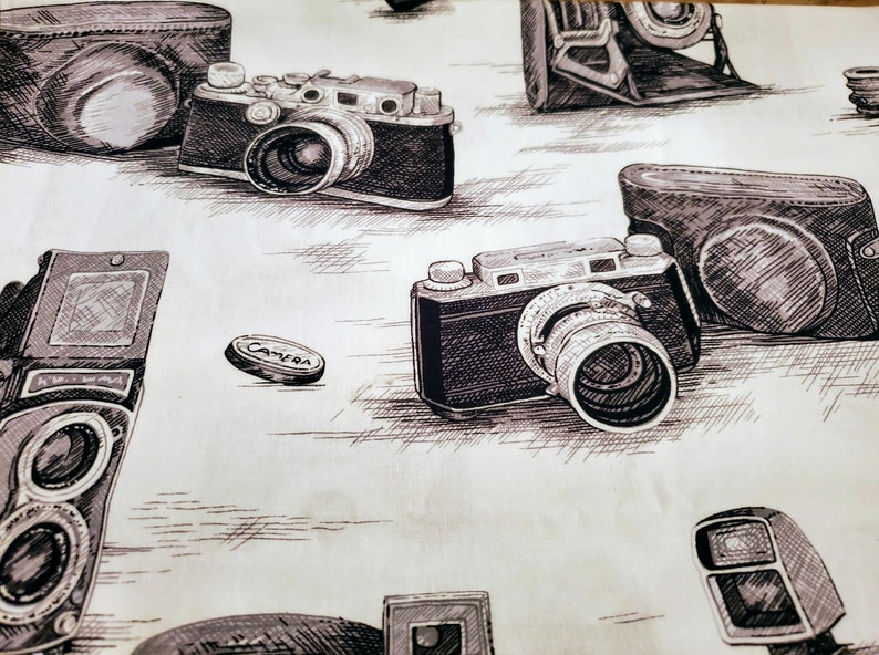 Może przedstawiać: Wz&oacute;r tapety w stylu vintage z r&oacute;żnymi rodzajami aparat&oacute;w fotograficznych, w tym aparatem 35 mm, dalmierzem i vintage'owym aparatem filmowym. Aparaty są narysowane w czerni i bieli na jasnobeżowym tle.