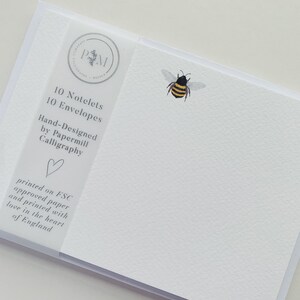 May include: A pack of white notecards and envelopes, each featuring a watercolour bee design. The set contains 10 notelets and 10 envelopes. The packaging states: "Hand-Designed by Papermill Calligraphy" and "printed on FSC approved paper and printed with love in the heart of England."