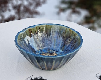 May include: A small, blue and green ceramic bowl with a rippled edge. The bowl has a unique, marbled glaze.