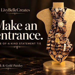 May include: A black and gold paisley patterned necktie displayed on a gold-toned stand. The tie features a decorative brooch, a gold safety pin with dangling charms, and a small white bead accent. Text on the image reads LivyBelleCreates, Make an entrance, ONE-OF-A-KIND STATEMENT TIE, and Black & Gold Paisley.