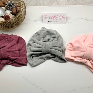 May include: Three turban headbands with large bows. The headbands are in shades of pink, grey, and burgundy.