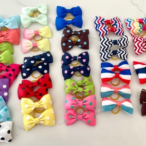 May include: A collection of 20 colourful hair bows with various patterns, including polka dots, stripes and zigzags. The bows are made of ribbon and have elastic bands.