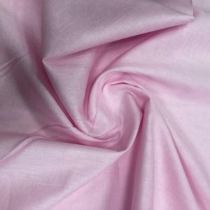 May include: A soft, pale pink fabric with a smooth, slightly textured surface. The fabric is draped and folded, creating a gentle, flowing effect.