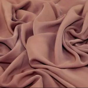 May include: A close-up of a soft, smooth, mauve fabric. The fabric is draped and folded, showing its texture and colour.