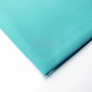 Op de afbeelding: Een gevouwen stuk turquoise blauwe stof. De stof is glad en heeft een lichte glans.