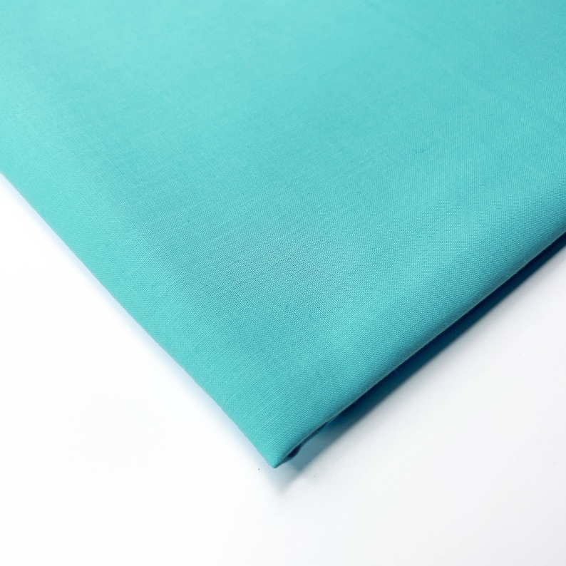 Op de afbeelding: Een gevouwen stuk turquoise blauwe stof. De stof is glad en heeft een lichte glans.