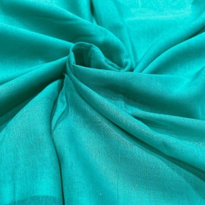 May include: A close-up of a teal fabric with a smooth, silky texture. The fabric is folded and draped, creating soft folds and curves.