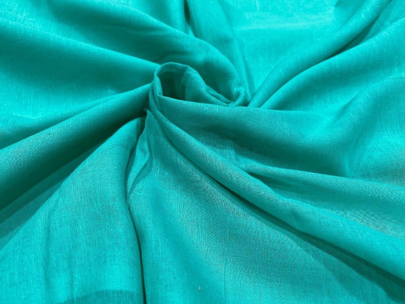 May include: A close-up of a teal fabric with a smooth, silky texture. The fabric is folded and draped, creating soft folds and curves.
