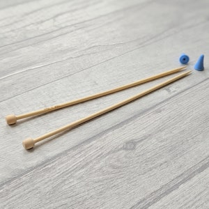 May include: Two wooden knitting needles with natural colored tips, and two blue plastic needle stoppers.