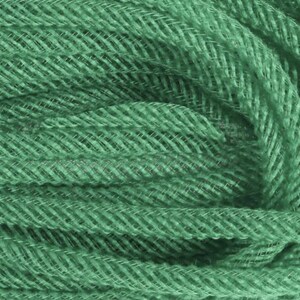 May include: Close-up of a bundle of sage green yarn. The yarn has a woven, textured appearance with a subtle herringbone pattern. The yarn is tightly wound, creating a dense, compact form, ideal for crafting projects.