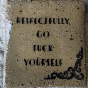 Op de afbeelding: Een vierkant, gespikkeld beige keramieken wandbord met twee metalen draadlussen aan de bovenkant. De tekst "RESPECTFULLY, GO FUCK YOURSELF" is gedrukt in zwarte, schreefloze letters, met een zwarte decoratieve krul in de rechterbenedenhoek.