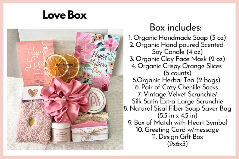 May include: A pink and white gift box filled with various items, including a pink scrunchie, a clay face mask, a soy candle, a card that says "Happy Mother's Day", and a soap saver bag. The box includes a variety of other items, including herbal tea, orange slices, and chenille socks.