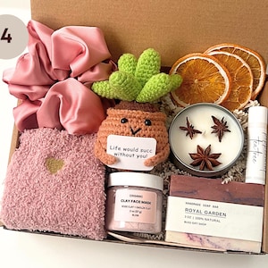 May include: A gift box filled with self-care items. Includes a pink scrunchie, fuzzy socks, a crocheted succulent, a candle, lip balm, a face mask, and a bar of soap. The succulent has a tag that reads "Life would succ without you!"