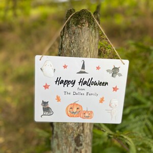 May include: White sign with the text "Happy Halloween from The Dallas Family" and illustrations of a ghost, witch's hat, bat, black cat, two jack-o'-lanterns, and a mummy.