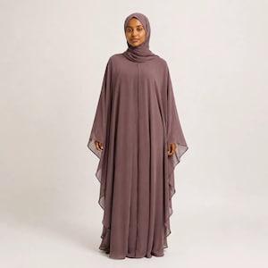 May include: A floor-length mauve abaya featuring a loose, flowing silhouette with wide, draped sleeves and a matching headscarf. The garment is constructed from a solid-coloured, opaque fabric that falls in vertical pleats from the neckline to the hem.