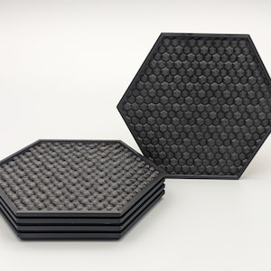 May include: Four black hexagonal coasters with a honeycomb pattern. The coasters are stacked on top of each other.