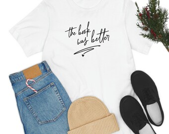 Pode incluir: Camiseta branca com o texto "the book was better" escrito em caligrafia preta.