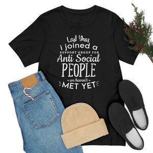 Puede incluir: Camiseta negra con texto blanco que dice "Last Year I joined a Support Group for Anti Social People =we haven't= MET YET"
