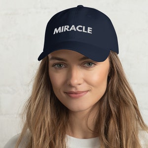 Puede incluir: Una gorra de béisbol azul marino con texto bordado en blanco que dice "MIRACLE".