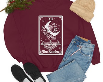 Puede incluir: Una sudadera de color granate con un gráfico blanco de una carta de tarot. La carta es la carta "El Lector" y presenta una luna creciente, cristales y una pila de libros.