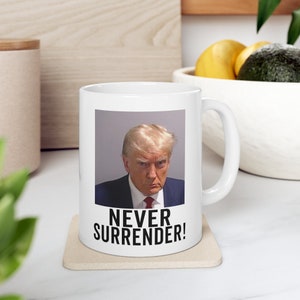 May include: White ceramic mug with a photo of Donald Trump and the text "NEVER SURRENDER!" printed on it.