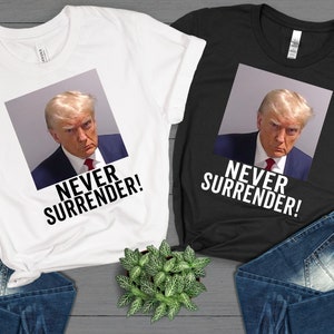 May include: Two t-shirts with a photo of Donald Trump and the text "Never Surrender!" printed on them. The t-shirts are white and black.