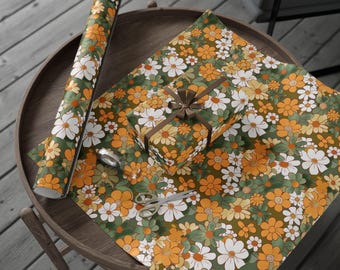 May include: A roll of green and orange floral wrapping paper with a white daisy pattern. The paper is rolled up and sitting on a wooden table next to a gift box wrapped in the same paper.