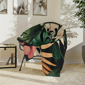 Può includere: Una coperta nera e verde con stampa tropicale con foglie grandi e fiori rosa. La coperta è drappeggiata su una sedia.