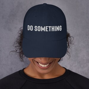 Könnte beinhalten: Eine marineblaue Baseballkappe mit weiß gesticktem Text, der "DO SOMETHING" lautet.