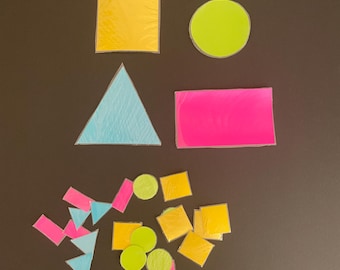 May include: An assortment of colorful geometric shapes, including squares, circles, triangles, and rectangles, in shades of yellow, green, pink, and blue. The shapes are arranged on a dark brown background, creating a visually engaging composition.