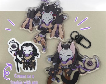 May include: Two clear acrylic keychains featuring a cartoon character with a white mask and purple accents. The character is holding a staff with a purple orb. The text "Comes as a freebie with any order!" is visible in the image.