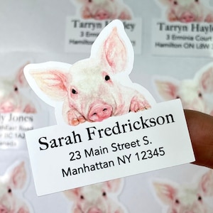 May include: A set of personalized return address labels featuring a cute cartoon piglet peeking over the top of a white label. The label reads "Sarah Fredrickson, 23 Main Street S., Manhattan NY 12345".