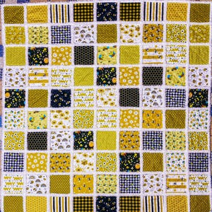 May include: A square rag quilt featuring a grid of alternating fabric patches in yellow, black, and white. The patterns include honeycombs, bumblebees, daisies, stripes, and gingham checks, all joined with frayed white seams between squares.