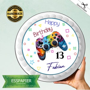 Könnte beinhalten: Ein runder weißer Kuchen mit einem essbaren Bild eines bunten Videospiel-Controllers, den Worten "Happy Birthday", der Zahl "13" und dem Namen "Fabian".