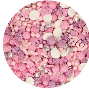 Könnte beinhalten: Eine Mischung aus rosa, weißen und silbernen Streuseln in kreisförmiger Anordnung. Die Streusel umfassen kleine Kugeln, Herzen, Kronen und andere Formen, ideal zum Dekorieren von Backwaren. Die Farbpalette ist hauptsächlich rosa, mit Akzenten in Weiß und Silber.