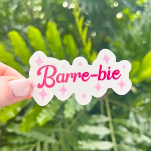 May include: A white sticker with pink glitter and the text "Barre-bie" in pink cursive font.