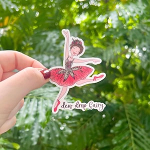 May include: A sticker featuring a ballerina with a pink and green floral tutu. The ballerina is wearing a flower crown and has a pink bow in her hair. The sticker has the text "dew drop fairy" written below the ballerina.