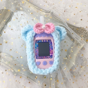May include: A light blue, plush, crocheted case for a handheld electronic device, shaped like a bubble tea cup. It features a pink bow with a pearl accent and a pink and purple device with a screen and buttons. The device has Chinese text.