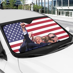 May include: A car windshield sunshade featuring an American flag with a group of people in front of it. The people are wearing suits and are looking at the camera. The sunshade is made of a durable material and is designed to protect your car's interior from the sun's harmful rays.