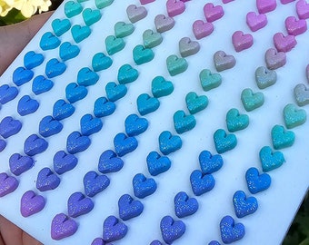 May include: A sheet of white paper with rows of iridescent heart-shaped stickers in shades of pink, blue, and purple.