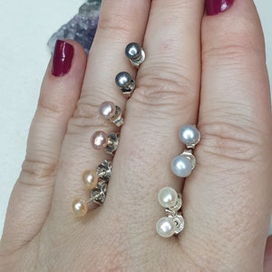 May include: A set of pearl earrings in various colors, including white, gray, and pink. The earrings are displayed on a hand, with the pearls facing the camera.