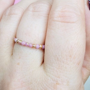 May include: A delicate pink and gold beaded ring. The ring is made of small, faceted pink beads and gold beads.
