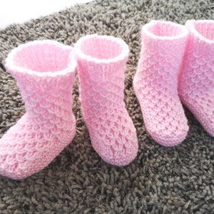 Puede incluir: Cuatro botines de bebé de punto rosa con un patrón texturizado. Los botines están sobre una alfombra gris.