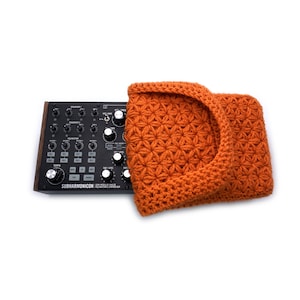May include: A black and silver synthesizer with knobs and buttons. The synthesizer is labeled "Subharmonicon" and is partially covered by an orange crocheted hat.